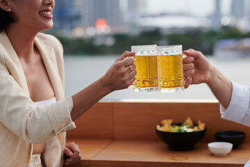 Cropped image of positive couple clinking mugs of cold beer