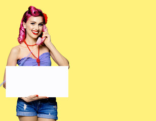 Woman with phone, in pinup cloth, showing blank white signboard with mock up copy space free text area, yellow background. Red purple hair girl pose in retro fashion vintage studio concept.