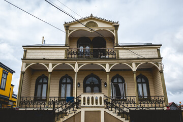 Three story old centuries cream wood house with stone basement and balconies and arches in a cloudy day, Valdivia, Chile