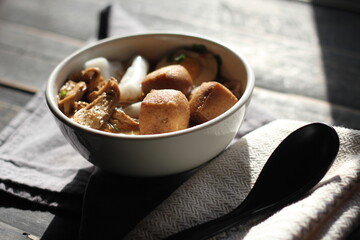 Rolled Rice Noodles in Five-spices Broth served in a white cup on a black wooden table.