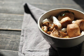 Rolled Rice Noodles in Five-spices Broth served in a white cup on a black wooden table.