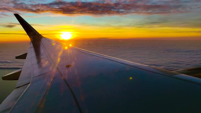 Airplane flying. Wing of an airplane flying above the clouds with sunset and sunrise sky. View from the window of the plane. Airplane, Aircraft. Traveling by air. 4K UHD video