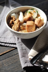 Rolled Rice Noodles in Five-spices Broth served in a white cup on a black wooden table.