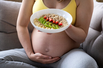 Belly of pregnant woman and plate with oatmeal and fruits. Nutrition and healthy diet during...