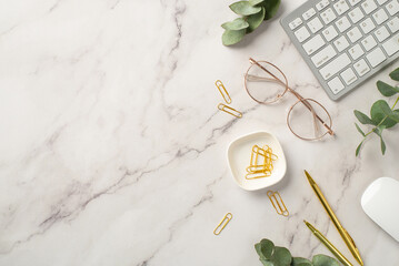 Business concept. Top view photo of workstation keyboard computer mouse gold pens clips glasses and eucalyptus on white marble background with empty space