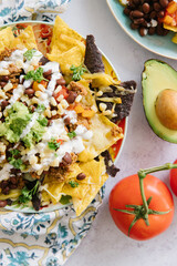 A plate of delicious plate of nachos. On the nachos is corn, avocado, salsa, tomatoes, chips, black beans, cheese and sour cream