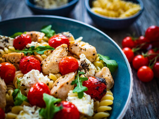 Roasted chicken nuggets, cherry tomatoes, feta cheese and fusilli  served on wooden table
