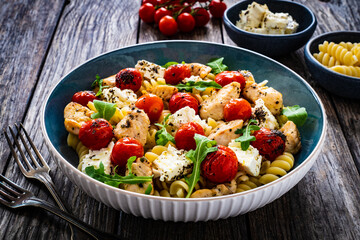 Roasted chicken nuggets, cherry tomatoes, feta cheese and fusilli  served on wooden table
