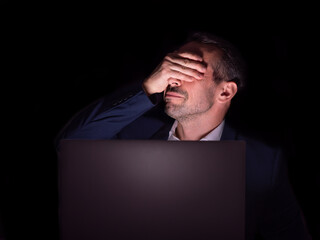 Frustrated businessman looking exhausted and covering his face with hand sitting at laptop