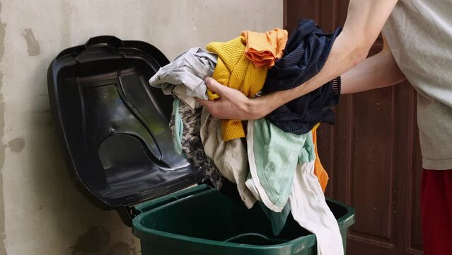 Clothing waste. The concept of fast fashion. A man throws old used clothes into a dumpster