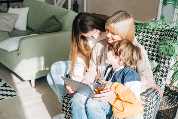 Family Mature senior woman mother with adult daughter and child kid boy using digital tablet computer device. Caucasian grandmother, daughter and grandson at home having online video conference call.