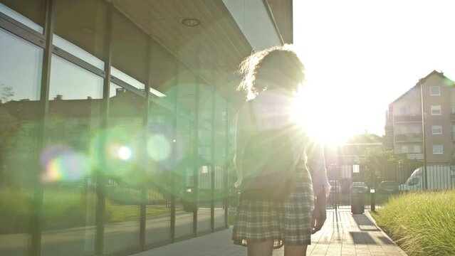 Teenage schoolgirl, college student, or high school student is returning from class. Back view.