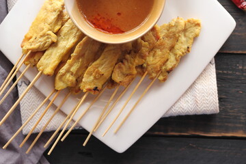 Pork satay served in a white plate with peanut and cucumber dipping sauce.