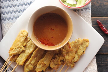 Pork satay served in a white plate with peanut and cucumber dipping sauce.