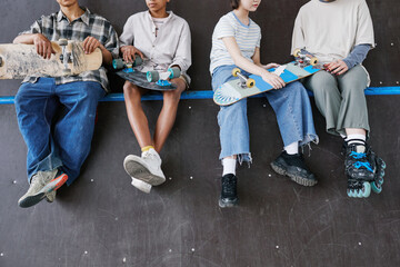 Diverse group of teenagers sitting on ramp in skateboarding park low section of feet dangling, copy space - Powered by Adobe