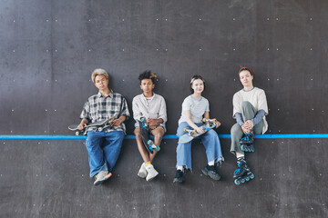 Minimal wide angle shot of diverse group of teenagers sitting on ramp in skateboarding park and...
