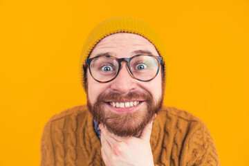 It's time to smile. Positive European lad showing his teeth in a big smile and intensively staring at camera white touching his beard over yellow background. High quality photo - obrazy, fototapety, plakaty