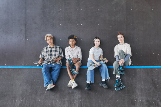 Minimal Wide Angle Shot Of Diverse Group Of Teenagers Sitting On Ramp In Skateboarding Park And Looking At Camera, Copy Space