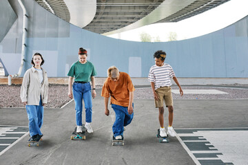 Full length shot of diverse group of teenagers riding skateboards in urban skating area, copy space