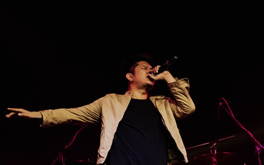 Asian male musical singer singing, celebrating, showing performance on stage in concert or event at night with spot light. Entertainment, Festival Concept.