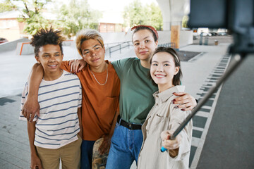 Diverse group of teens taking selfie photo outdoors in urban area using selfie stick