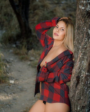 Plus size latina in re dplaid and black panties poses by a tree