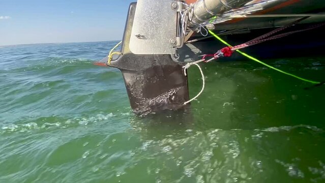 Rudder blade close up. Afterpiece of rudder. Part of catamaran control. Stern drive on boat. Steering device of sea and river vessels. Rear view of a sailboat floating on water.