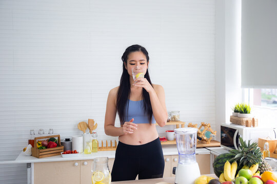 Fit And Healthy Young Asian Woman In Sportswear Preparing And Drinking Fresh Lemon Water For Healthy Lifestyle And Fitness In Modern Kitchen After Morning Workout And Exercise