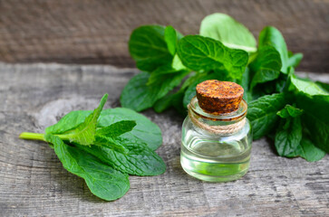 Peppermint essential oil in a glass bottle with fresh green mint leaves on old wooden table for spa,aromatherapy,homeopathy and bodycare.