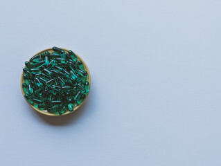 On a white background there is a plate with green capsules. Soft focus