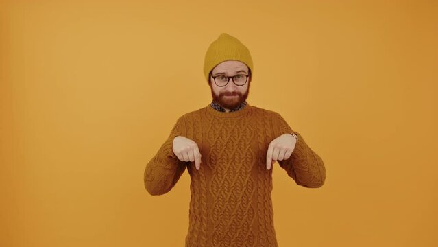 Check out the advertisement below. Bearded caucasian guy in a beanie pointing down to copy space over yellow background. High quality 4k footage