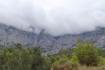 Fototapeta na wymiar Rain clouds hide the tops of the mountains, green pines against the background of gray rocks and clouds