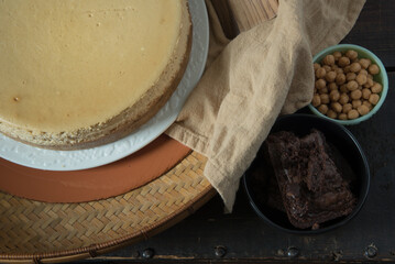 Top view cheesecake with topping options of caramels and brownie pieces on a dark wooden background.