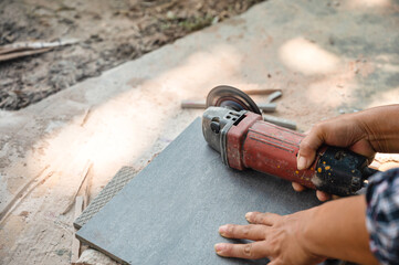 Worker using electric circular saw cutting tile in construction site