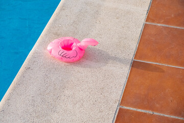 small pink flamingo float deflated on the edge of a swimming pool, summer time