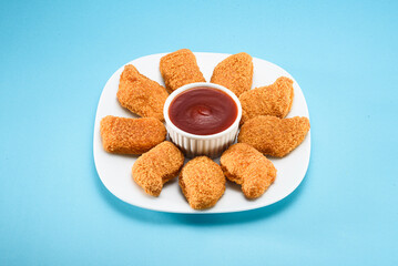 Chicken nuggets equally placed on a white plate, with ketchup on the middle, isolated on blue background