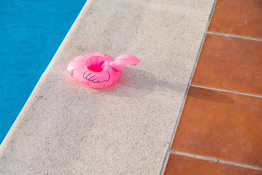 Small Pink Flamingo Float Deflated On The Edge Of A Swimming Pool, Summer Time