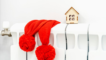 A model of a house wrapped in a scarf, on a radiator in the room, a place for text. Efficiency of...