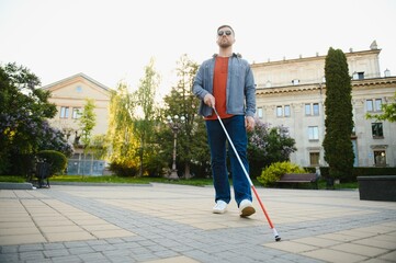 young blind man with white cane walking across the street in city