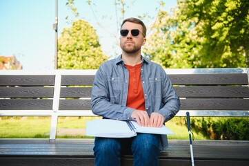 Blind man reading book on bench in park