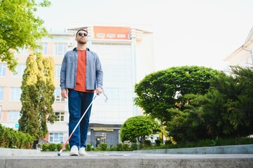 young blind man with white cane walking across the street in city