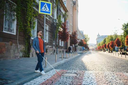 Blind person with white cane crossing street in city, closeup