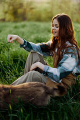 Happy woman sitting in nature and playing with her pet in the park sitting on the green grass 