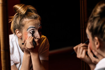 Female clown applying makeup in dressing room