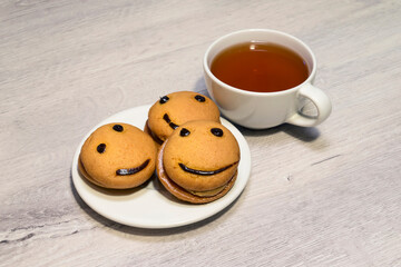 Smile cookies on a white plate with a cup of tea. Sweet biscuit. Tasty food.