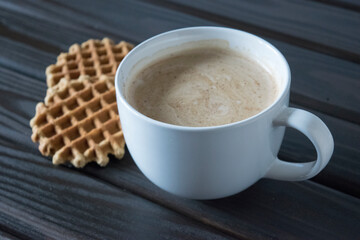 White cup and two wafers on wooden table.