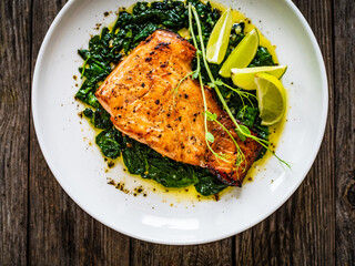 Fried salmon steak with spinach and lime served on wooden table
