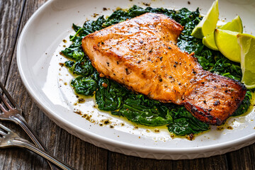 Fried salmon steak with spinach and lime served on wooden table
