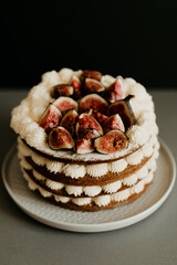 A fig cake with tea leaves in the sponge, lots of whipped cream decoration and fresh sliced figs on top. Gray plate and table, black background. Copy space.