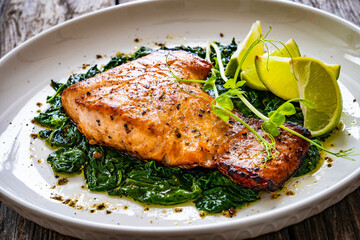 Fried salmon steak with spinach and lime served on wooden table
